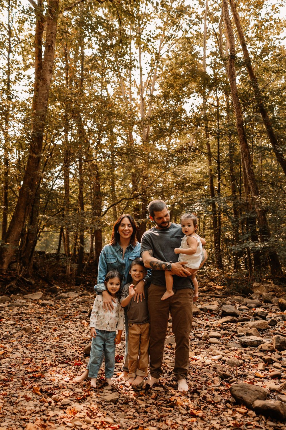 Happy family of five posing in autumn forest with fallen leaves and tall trees.