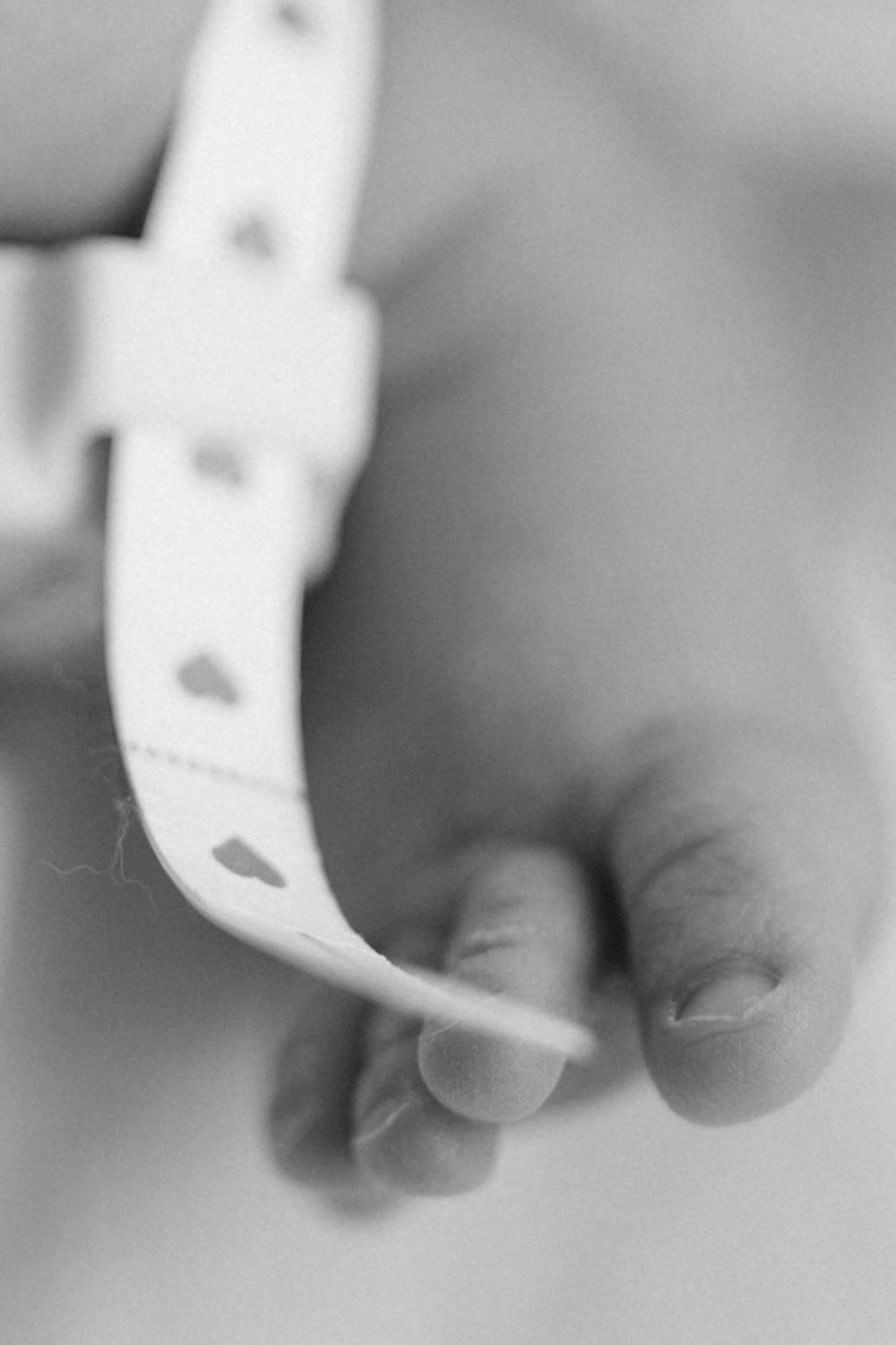 Black and white close-up of newborn baby foot wearing heart-patterned hospital identification bracelet.