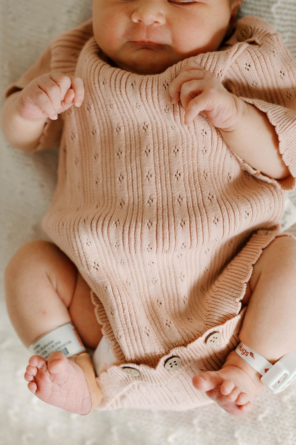 Close-up of a newborn baby in a pink knit romper lying on a soft white blanket.