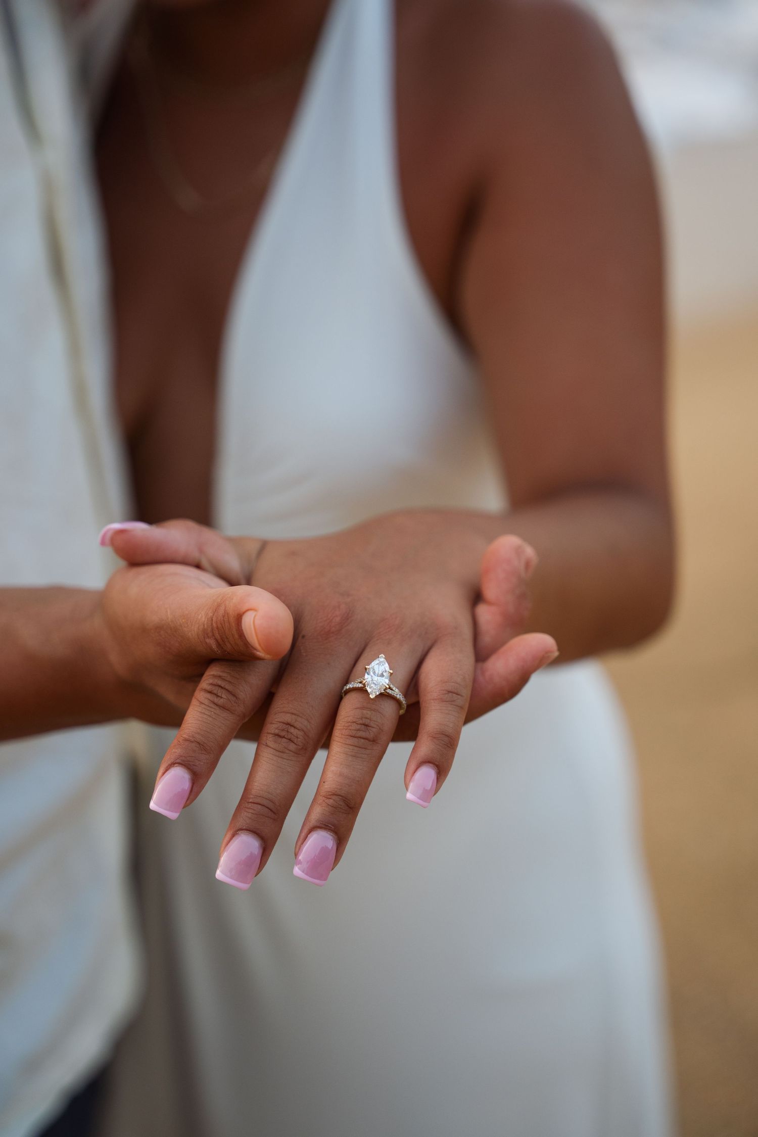 Close-up of an engagement ring with a marquise diamond on a woman's hand held by her partner outdoors.