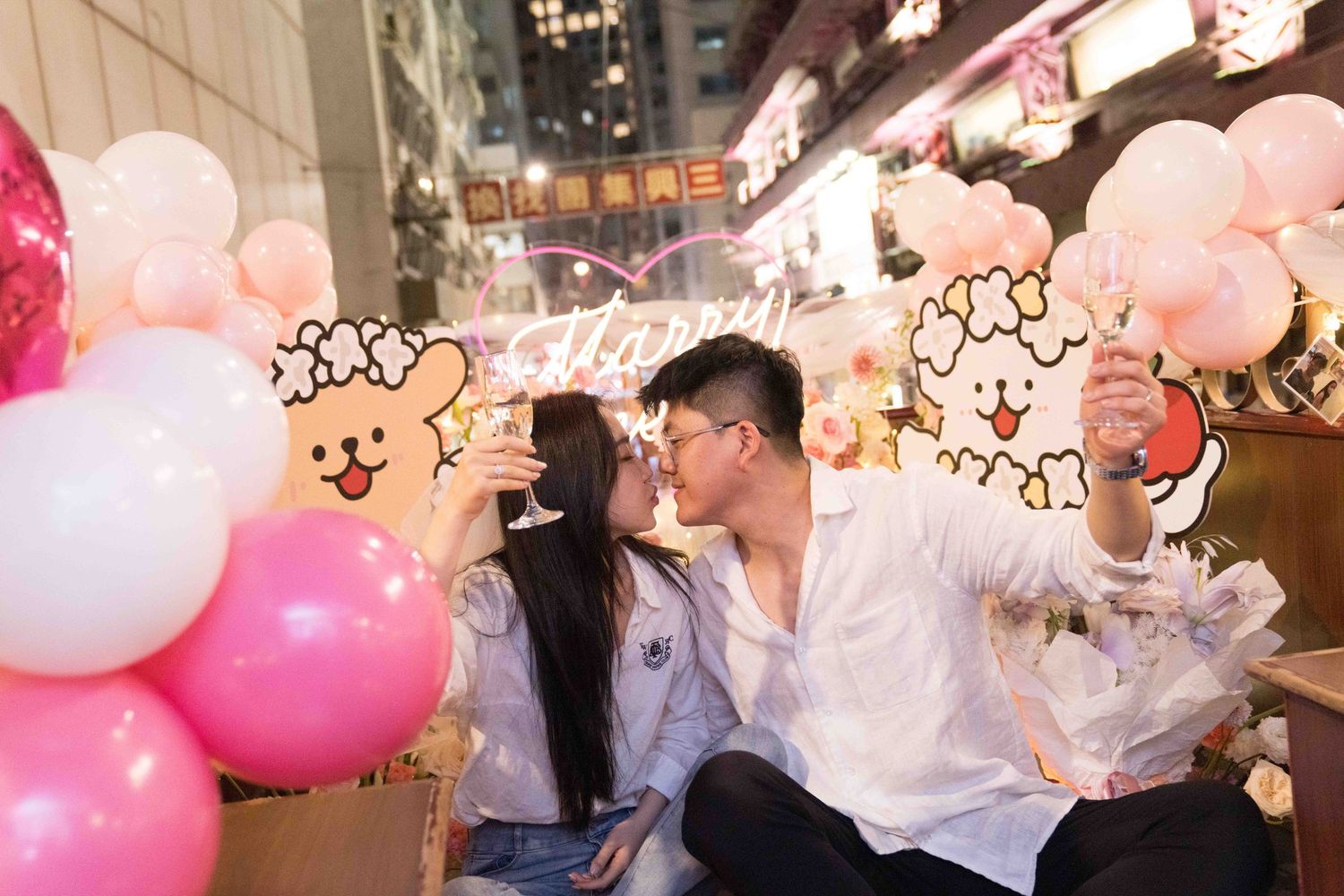 Crowd celebrates in city street with pink and white balloons creating a festive nighttime atmosphere.
