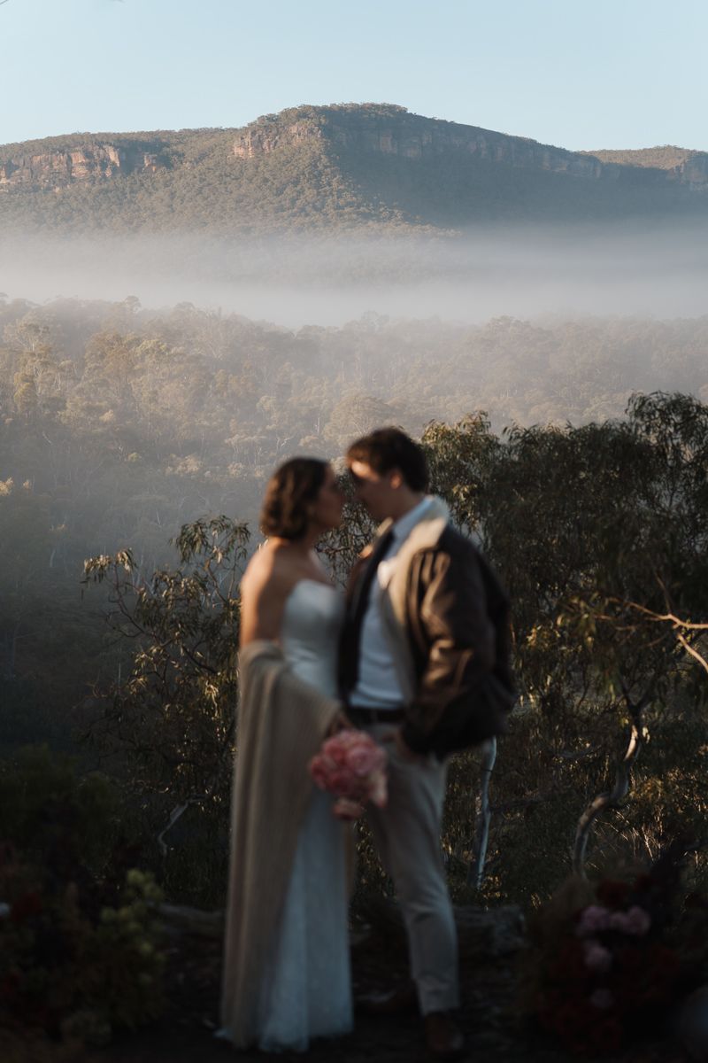 A bride and groom share an intimate moment overlooking a misty mountain valley landscape at golden hour, elopement photoshoot