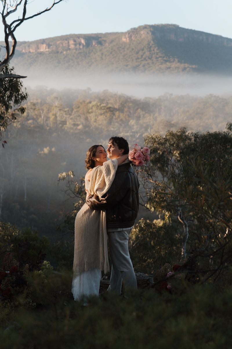 Couple embracing at misty Blue Mountains lookout, surrounded by lush eucalyptus forest and dramatic escarpment views, elopement photoshoot