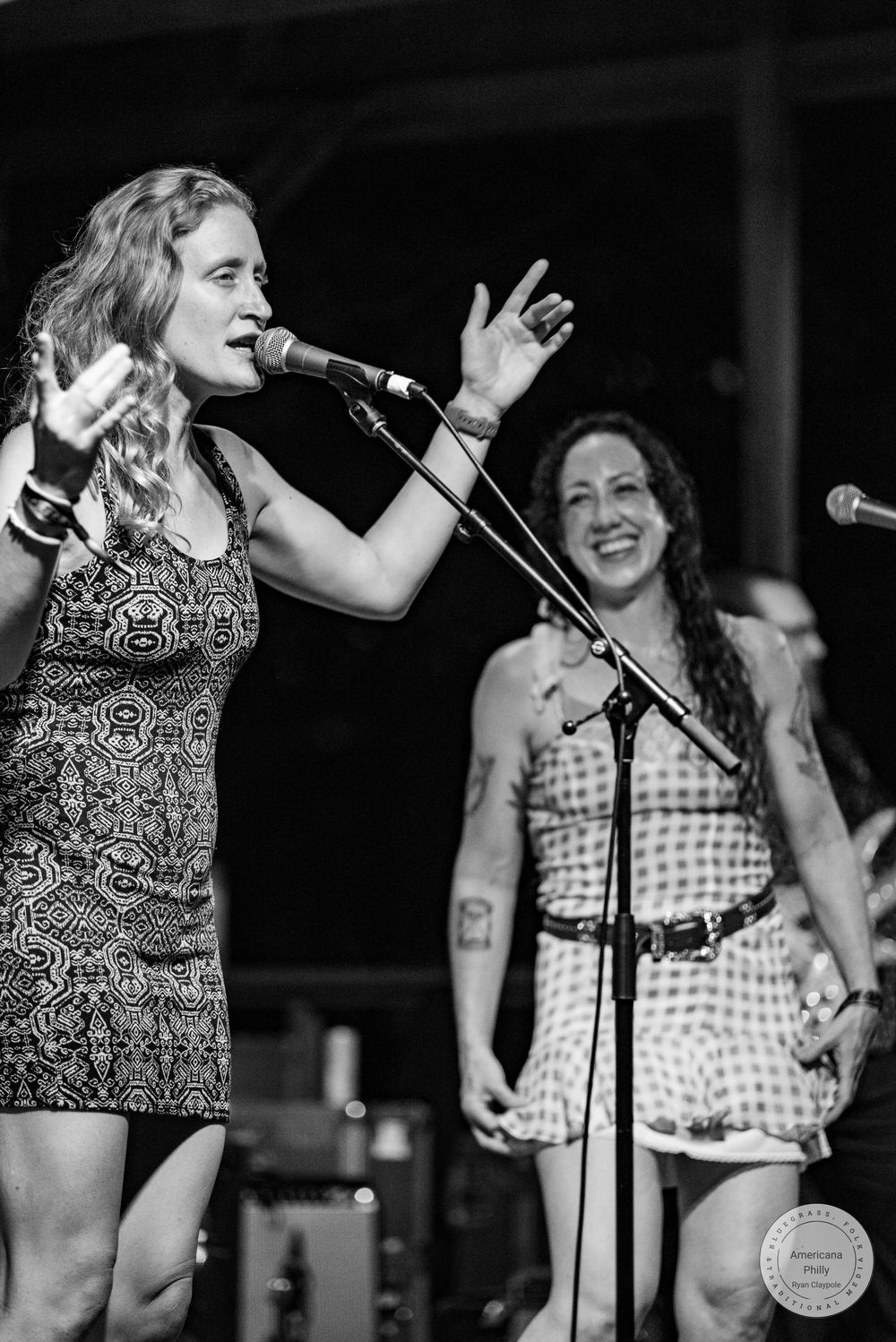 Two women performing on stage, one singing passionately into microphone at live music event.