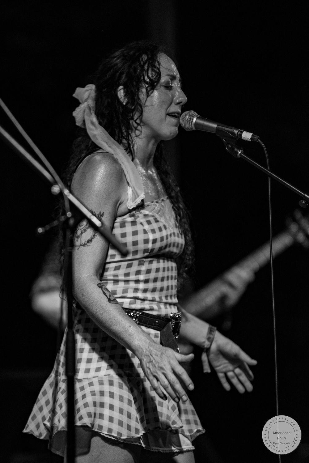 Black and white photo of a female singer performing on stage at a microphone in a checkered dress.