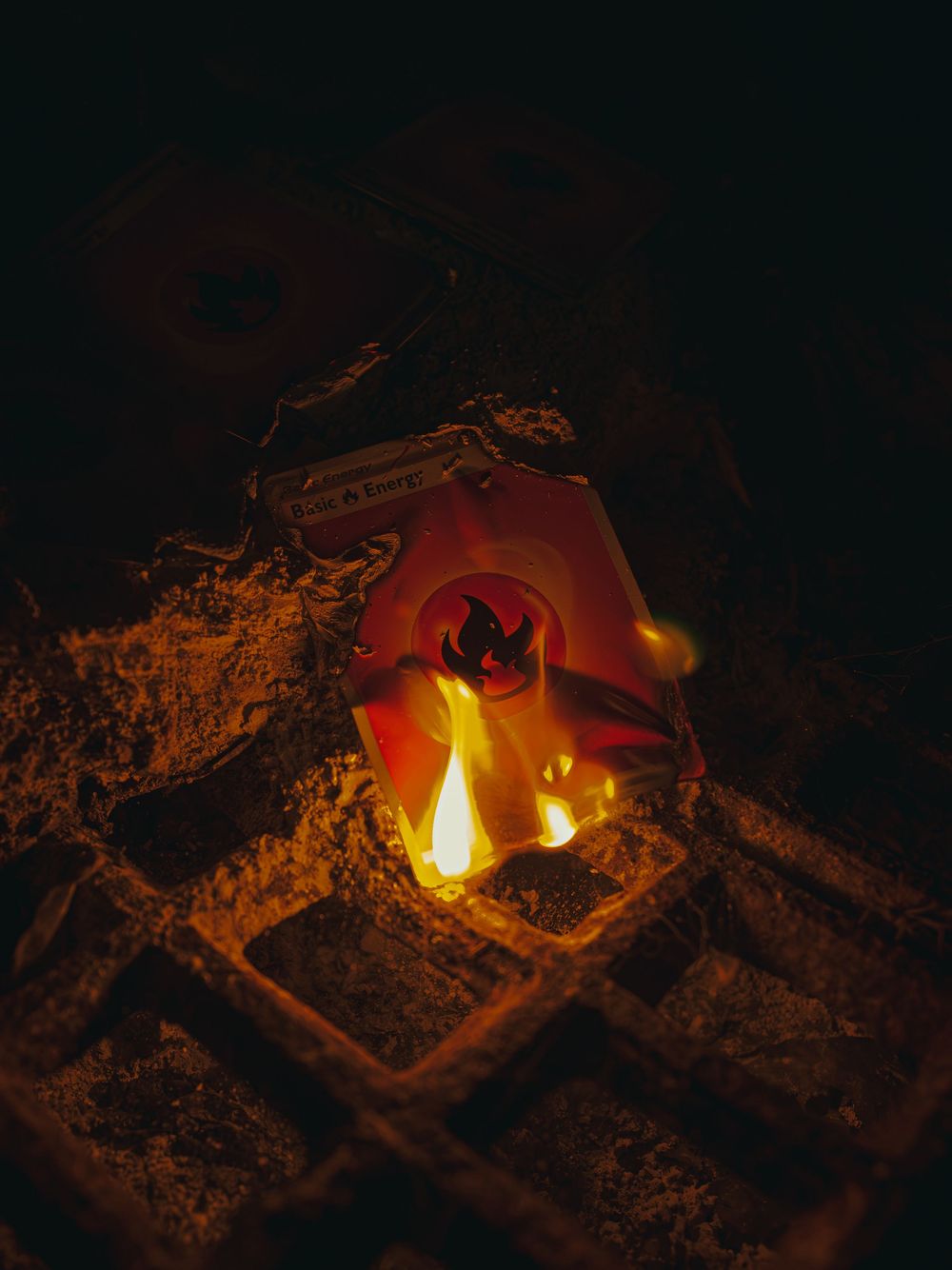 Product photograph of a fire-energy collectible card ablaze on a metal grate, yellow flames rising over its glossy surface in the dark.