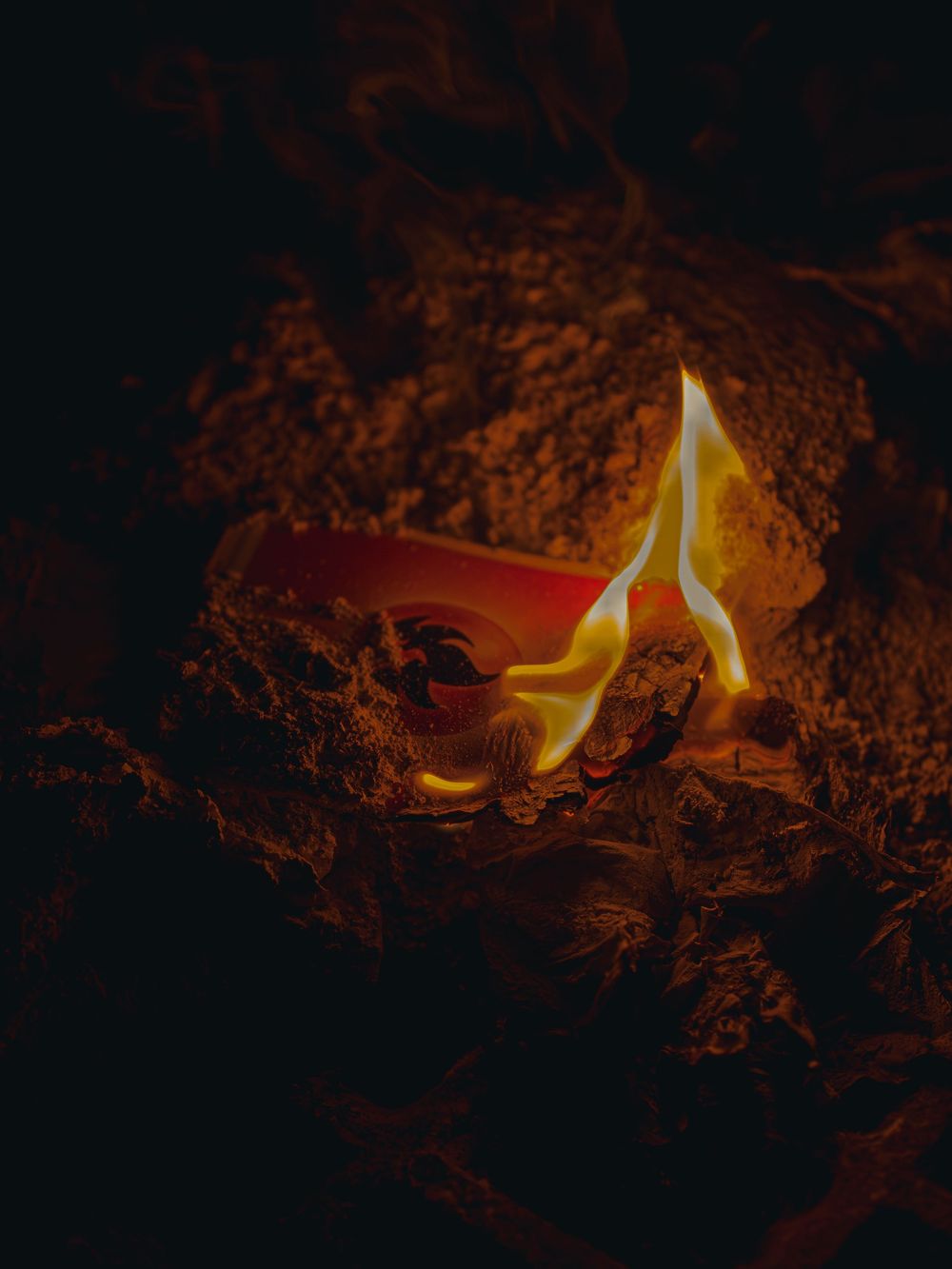 Close product photograph of a fire-energy collectible card half-buried in ash, a single tall flame rising from its glowing red surface.