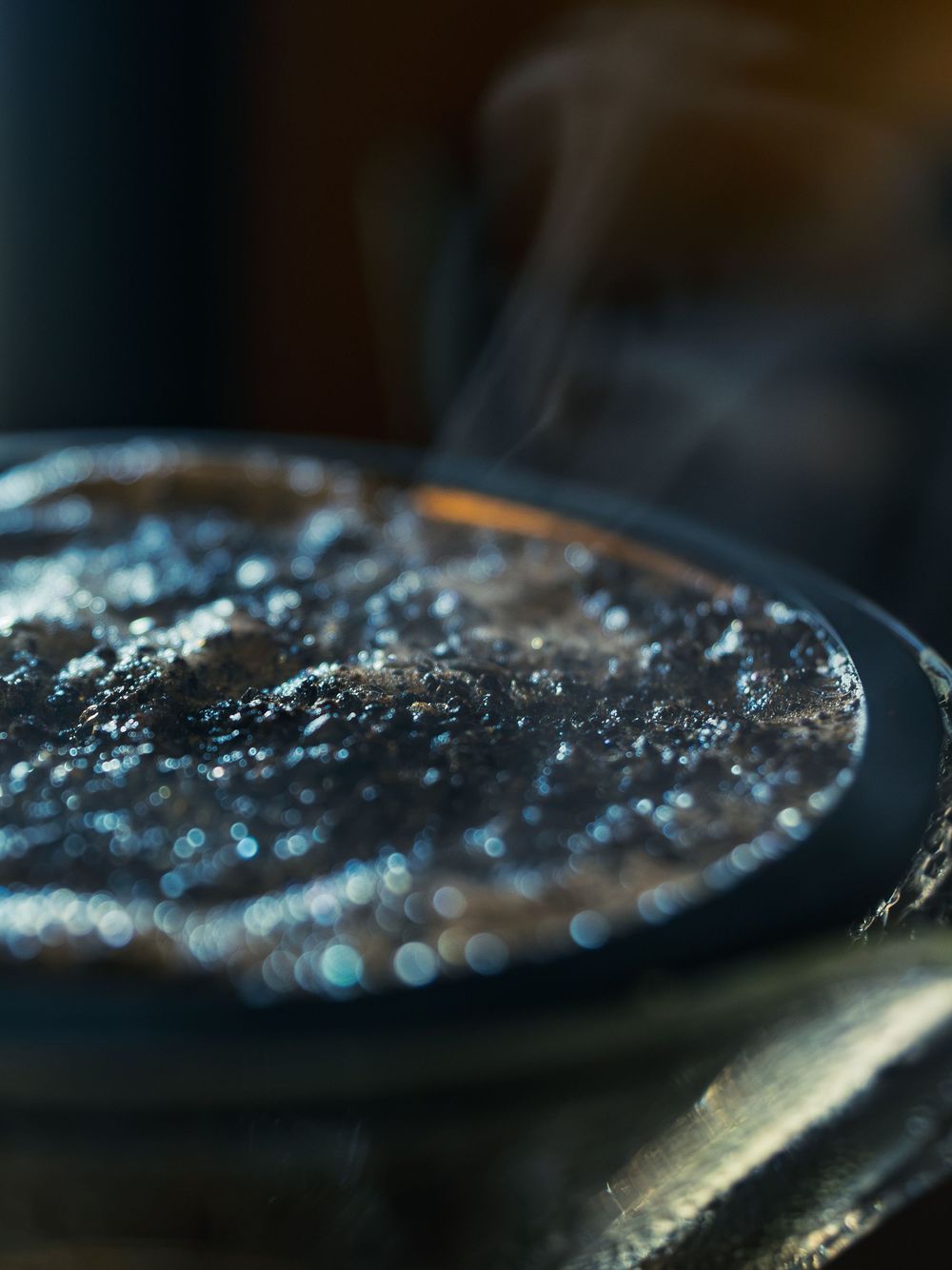 Macro close-up of steam rising off the bubbling surface of freshly brewed coffee, warm light catching the wet texture.