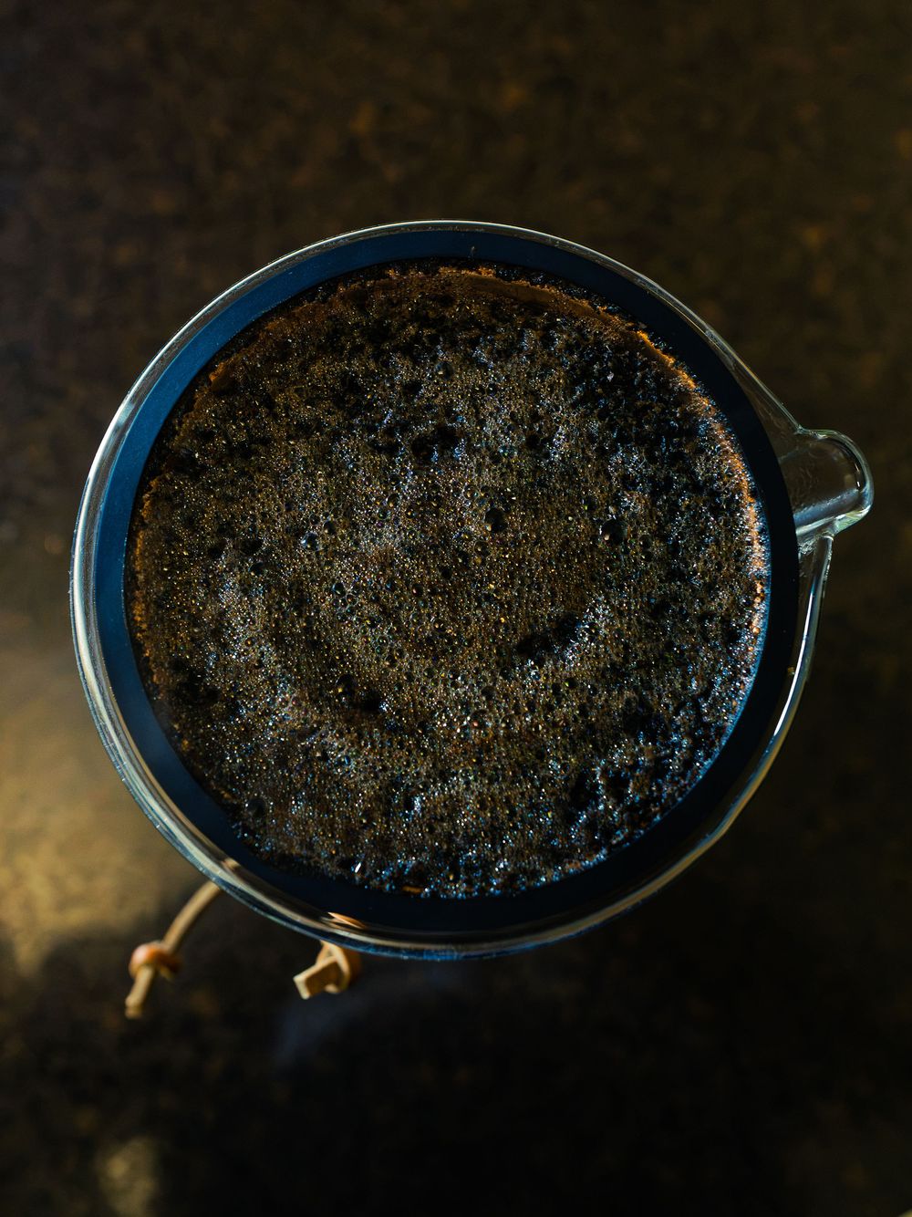 Overhead view of coffee blooming in a glass pour-over brewer, bubbles rising through the wet grounds as hot water saturates them.