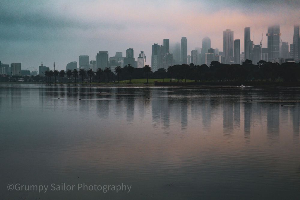The city emerges through the morning haze as still waters mirror Melbourne's skyline.