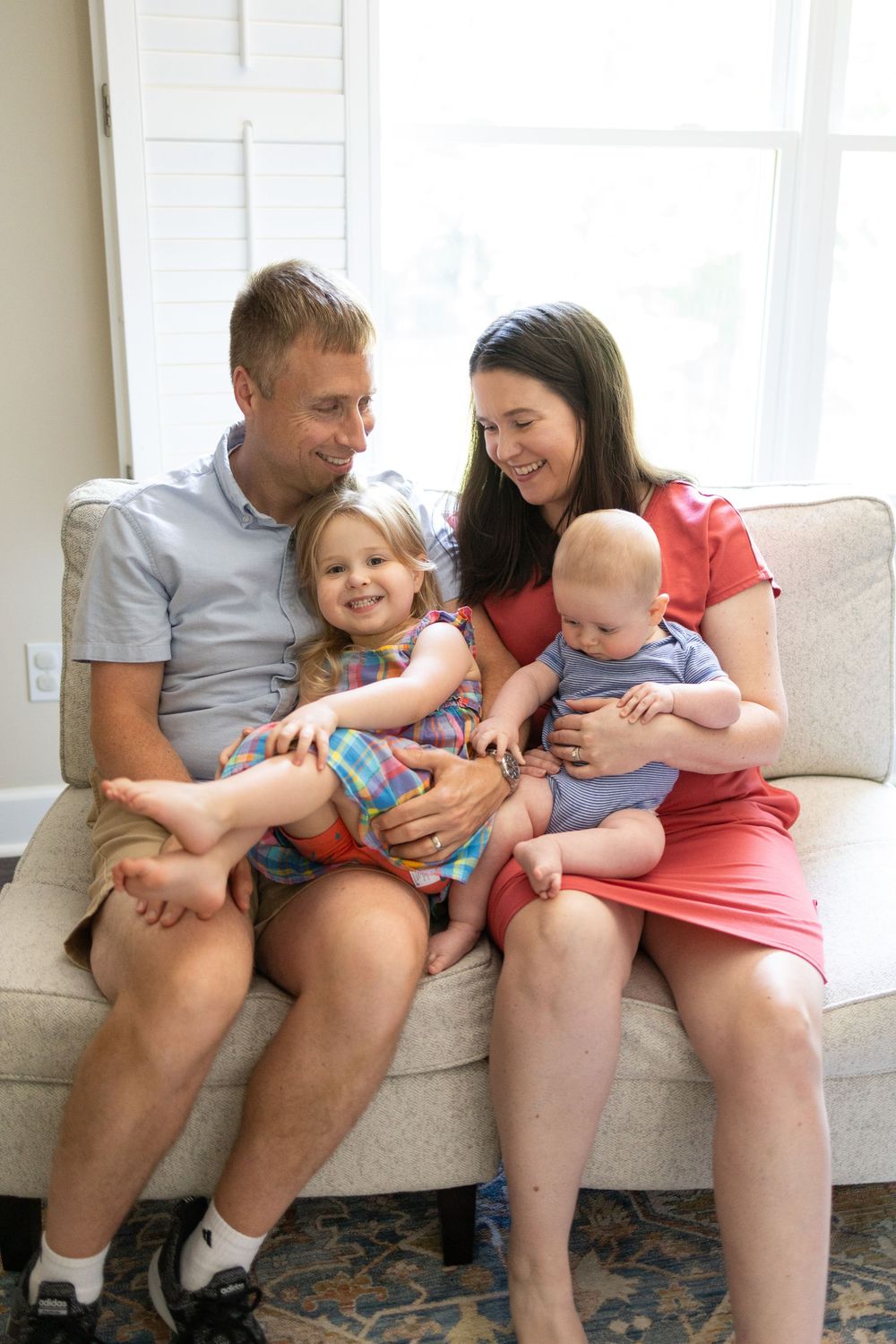 Smiling family of four with toddler girl and baby boy sitting on couch together.