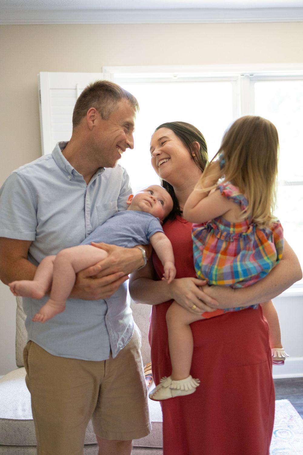 Joyful family of four with two young children laughing together in a bright, airy room.