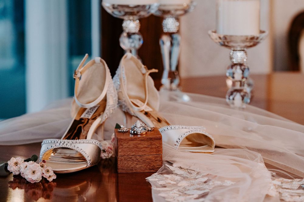 Elegant bridal heels with floral details displayed on a wooden box beside candlesticks and a lace veil.