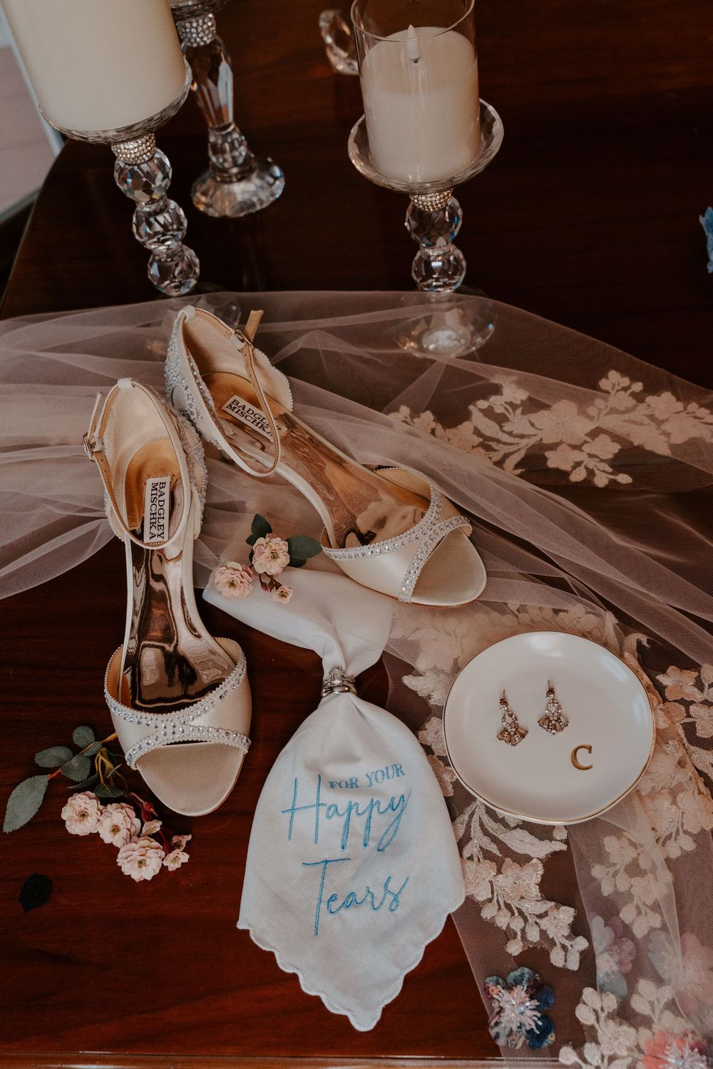 Bridal flat lay featuring Badgley Mischka heels, Happy Tears handkerchief, pearl earrings, and candles on a wooden table.