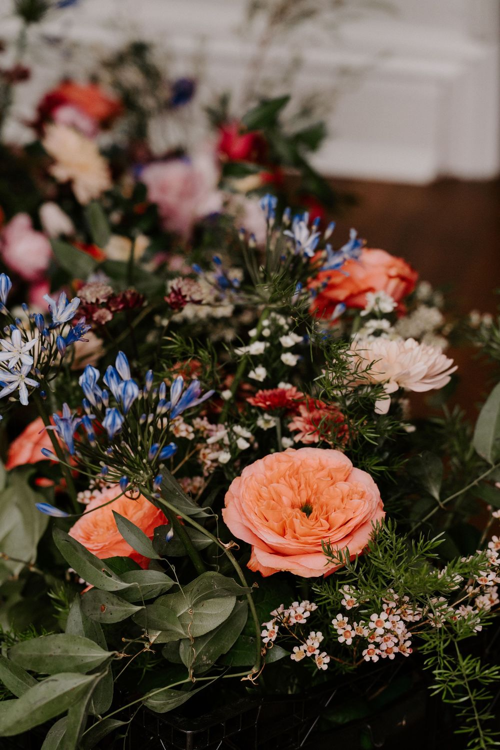 Lush wedding floral arrangement featuring peach garden roses, blue agapanthus, and wildflowers in rich jewel tones.