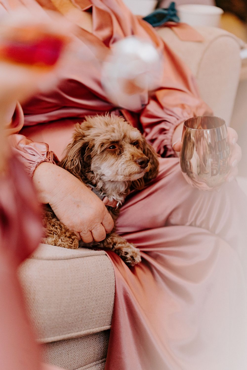 Bridesmaid in pink satin dress holding a glass while cradling an adorable fluffy brown dog in her lap.