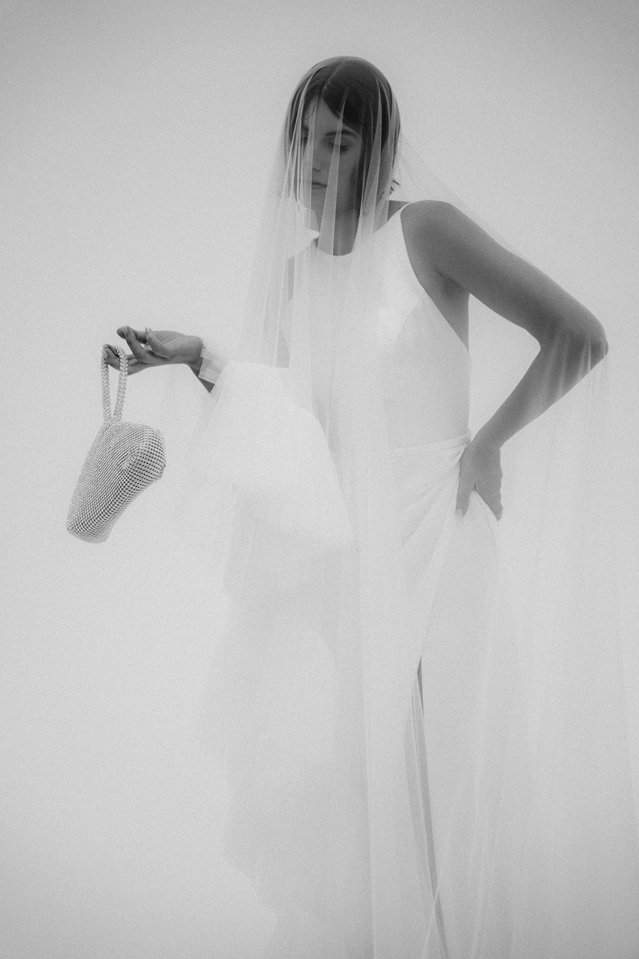 Black and white photo of a bride in a white gown and veil holding a beaded bag.