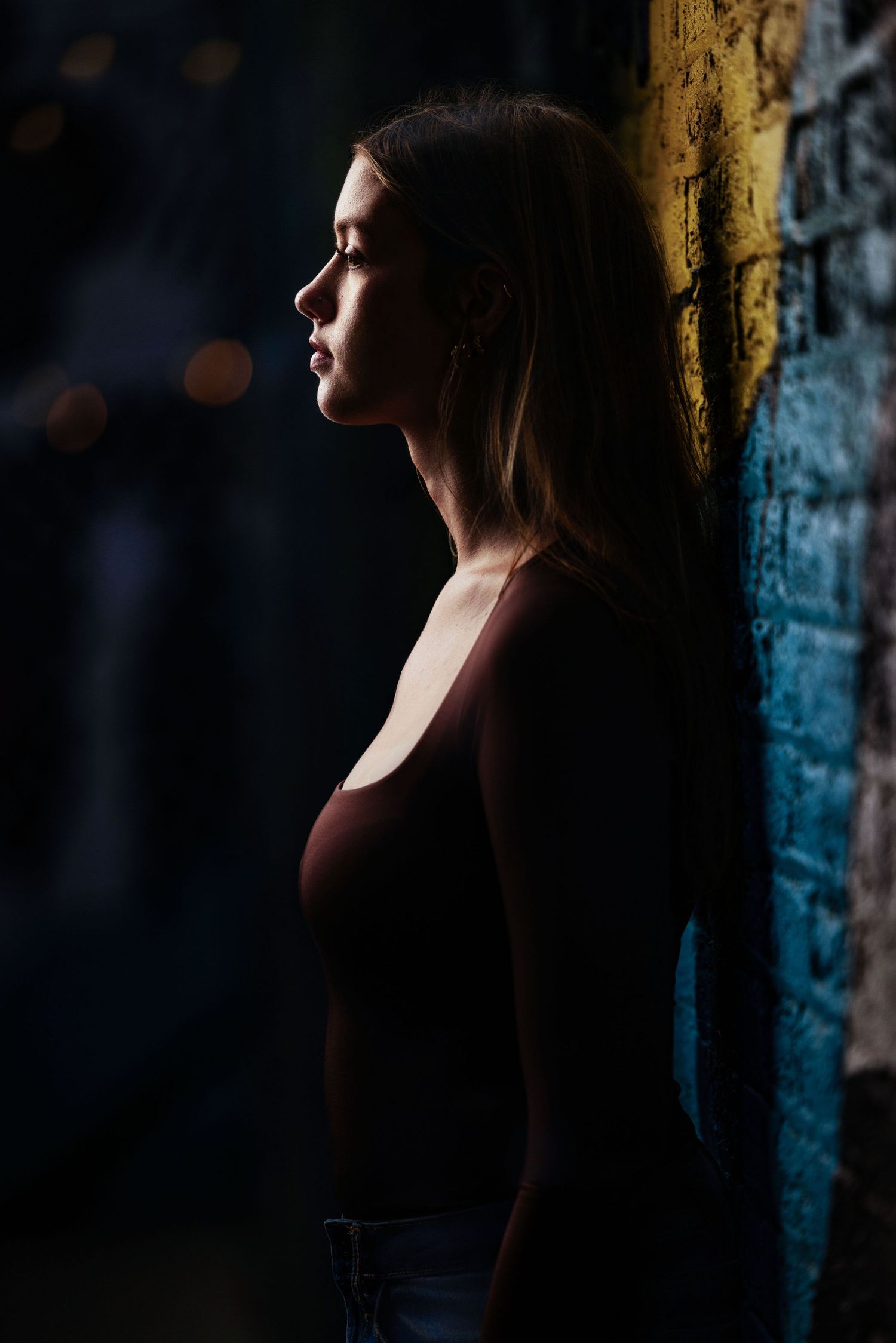 Dramatic profile senior portrait of a brunette girl beside a brick wall