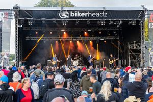 Rock band performing on Bikerheadz outdoor festival stage with large crowd.