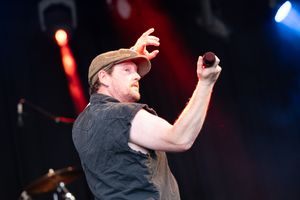 Male vocalist performing passionately with microphone at outdoor music festival stage.