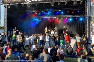 Rock band performing on Bikerheadz outdoor festival stage with crowd watching.