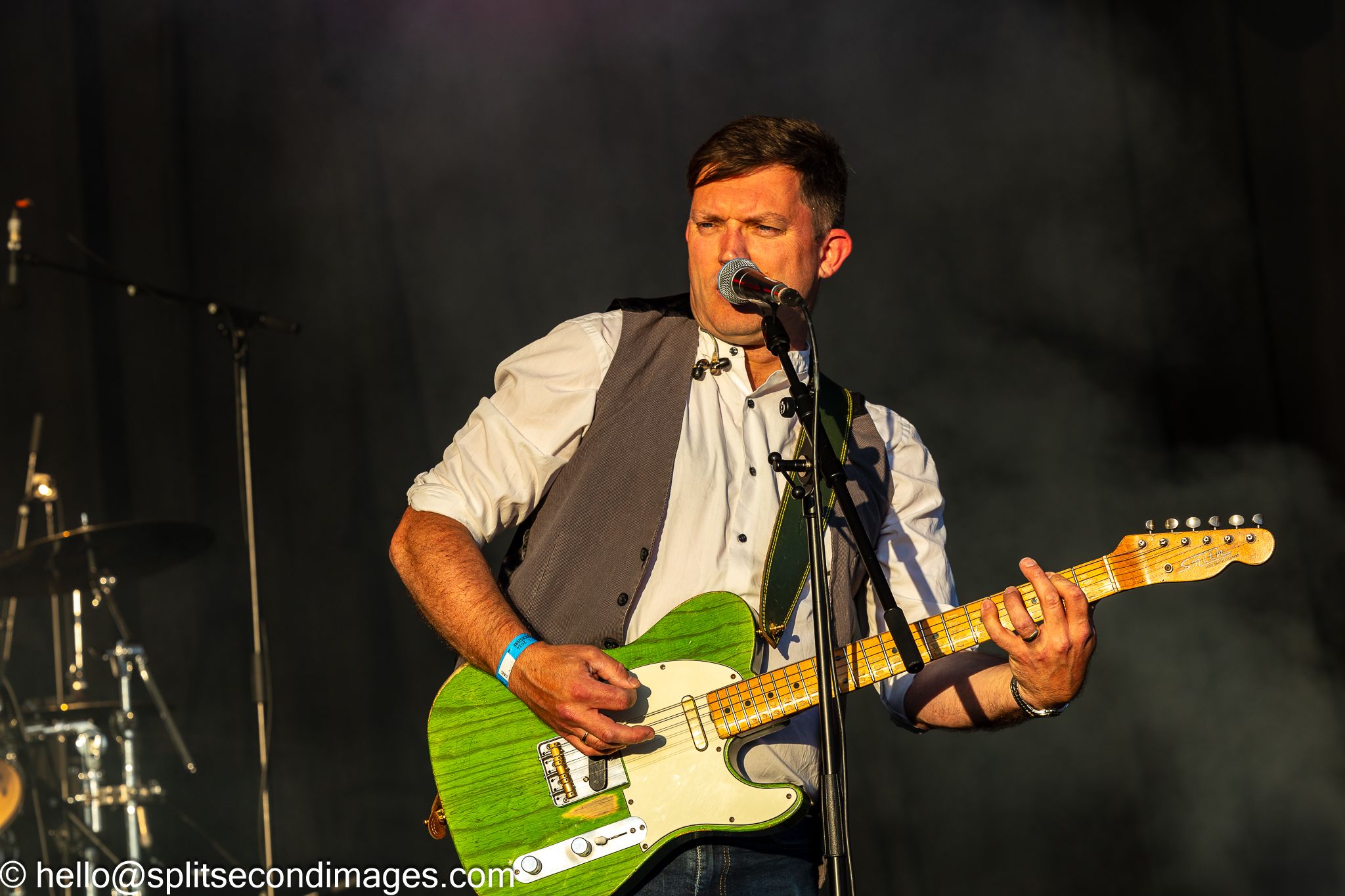 Male guitarist playing green Telecaster electric guitar and singing at outdoor music festival.