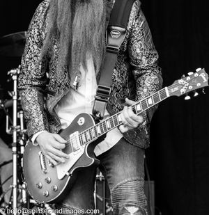 Black and white close-up of guitarist playing a Les Paul electric guitar in a sequined jacket.