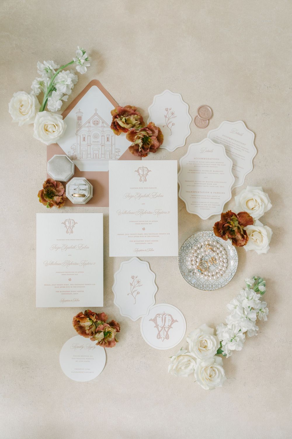 Elegant wedding invitation suite with white and blush stationery, pearl jewelry, and floral accents on a neutral background.