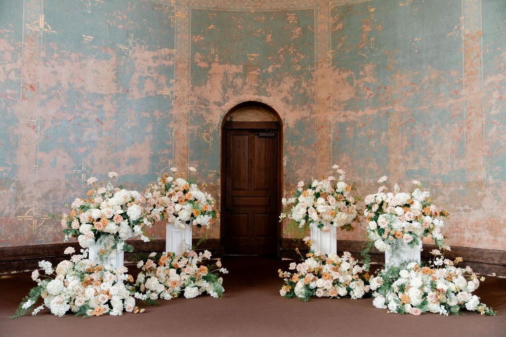 Elegant wedding altar with lush peach and white floral arrangements against a rustic distressed wall.