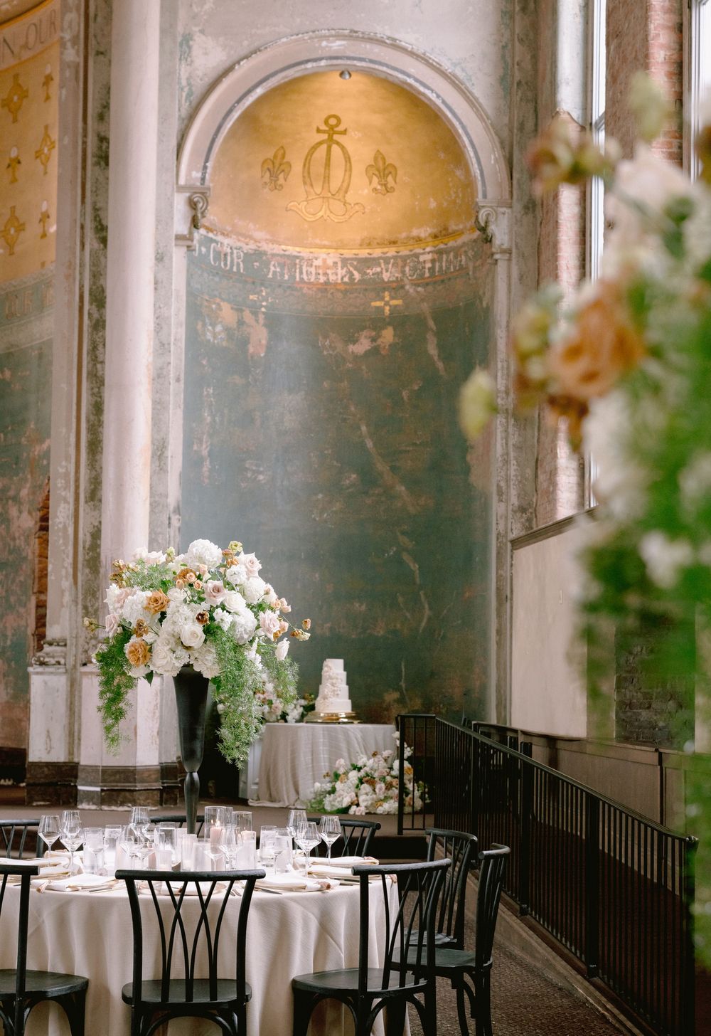Elegant wedding reception in historic venue with tall floral centerpieces, white tablecloths, and ornate golden mosaic arch backdrop.