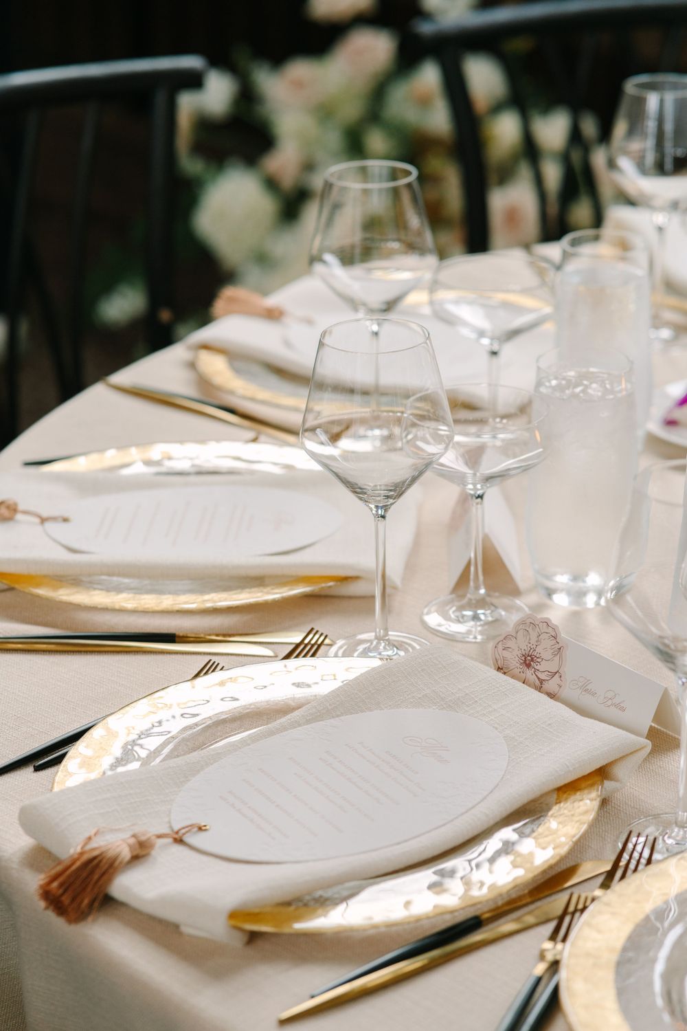 Elegant wedding reception table set with gold charger plates, crystal wine glasses, and tassel menus.