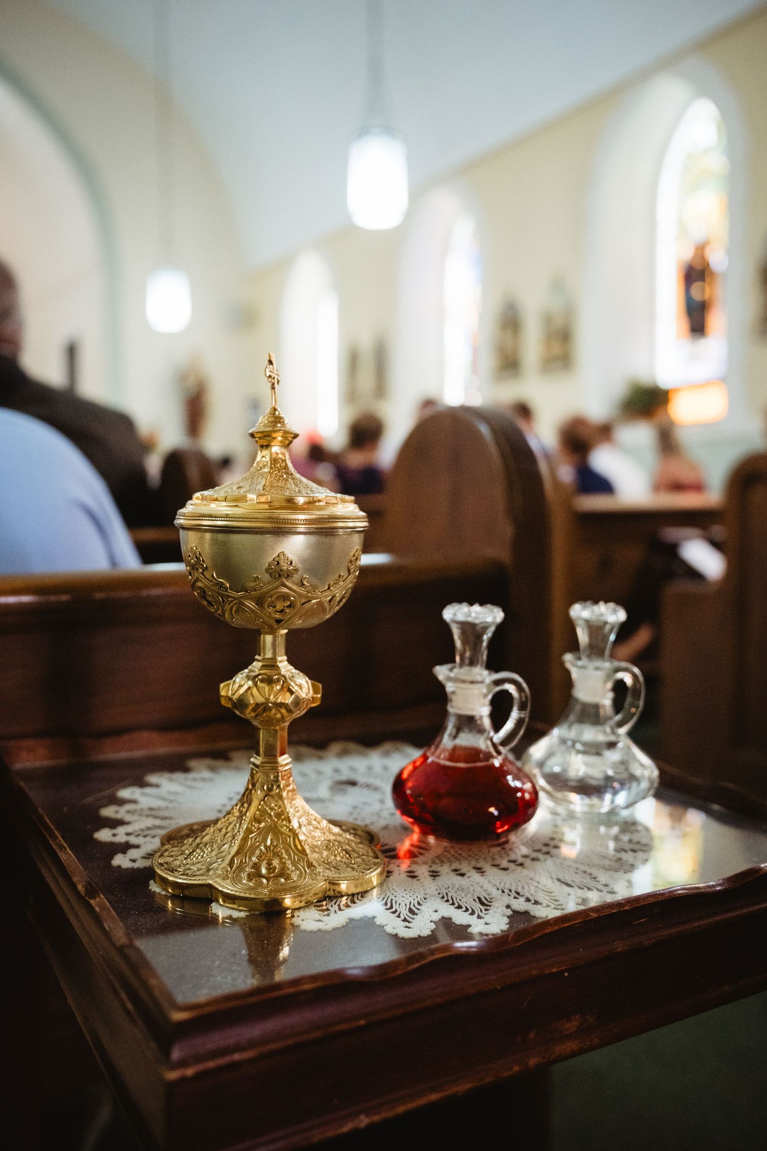 Golden ciborium and crystal cruets on lace cloth atop church pew during Catholic Mass ceremony.
