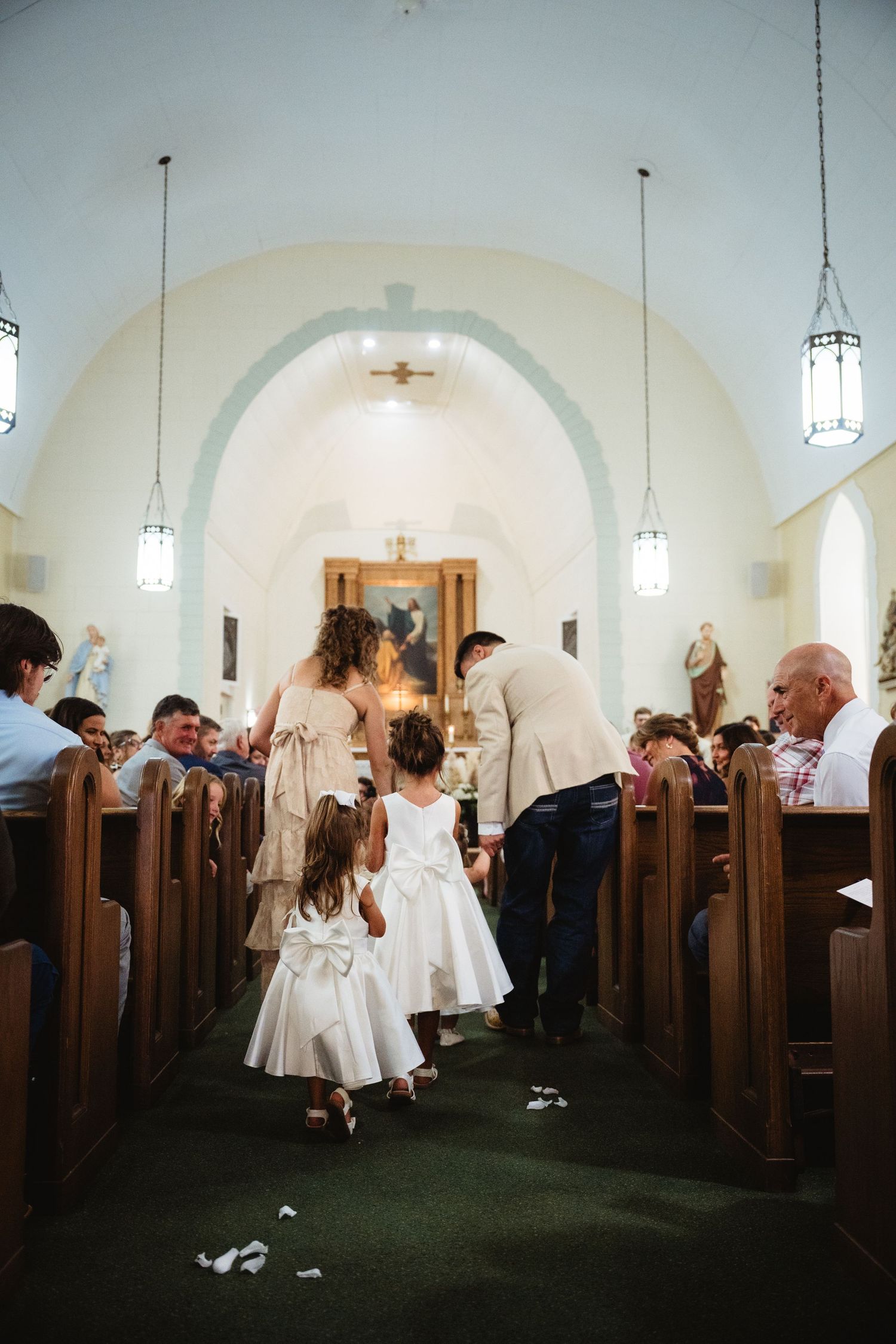 Two flower girls in white dresses walk down a church aisle during a wedding ceremony.