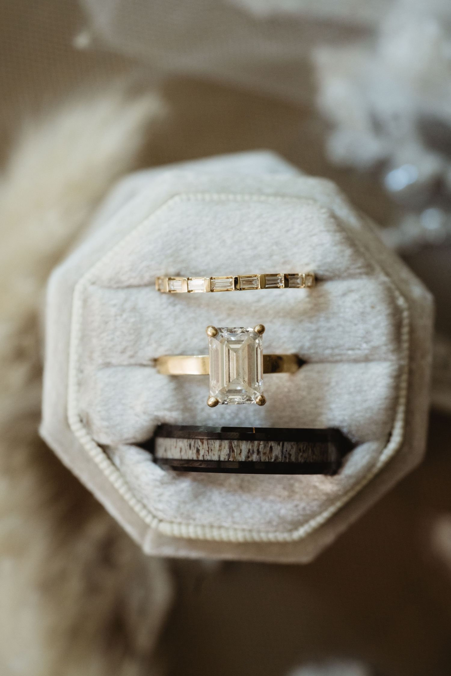 Elegant emerald cut diamond engagement ring with gold band and baguette diamond wedding band displayed in ivory velvet ring box.