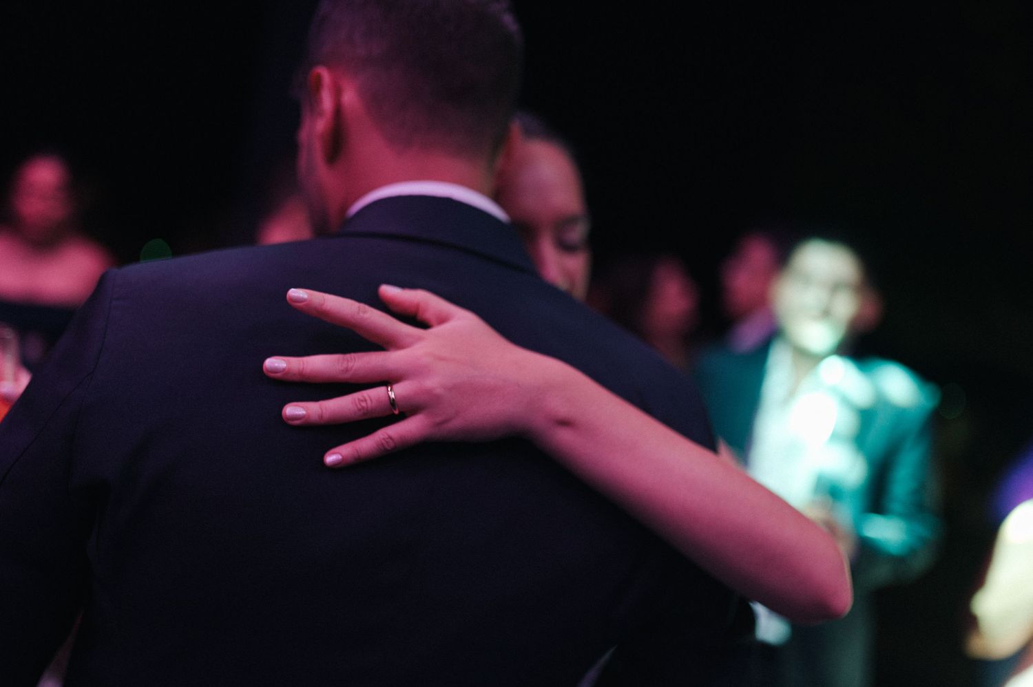 Couple sharing a slow dance embrace at a formal event, woman's hand resting on man's suited shoulder.