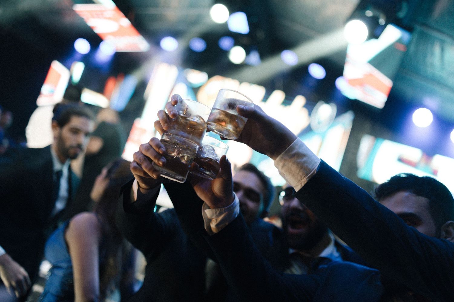 Group of people in formal attire toasting with glasses of whiskey at a glamorous evening event.