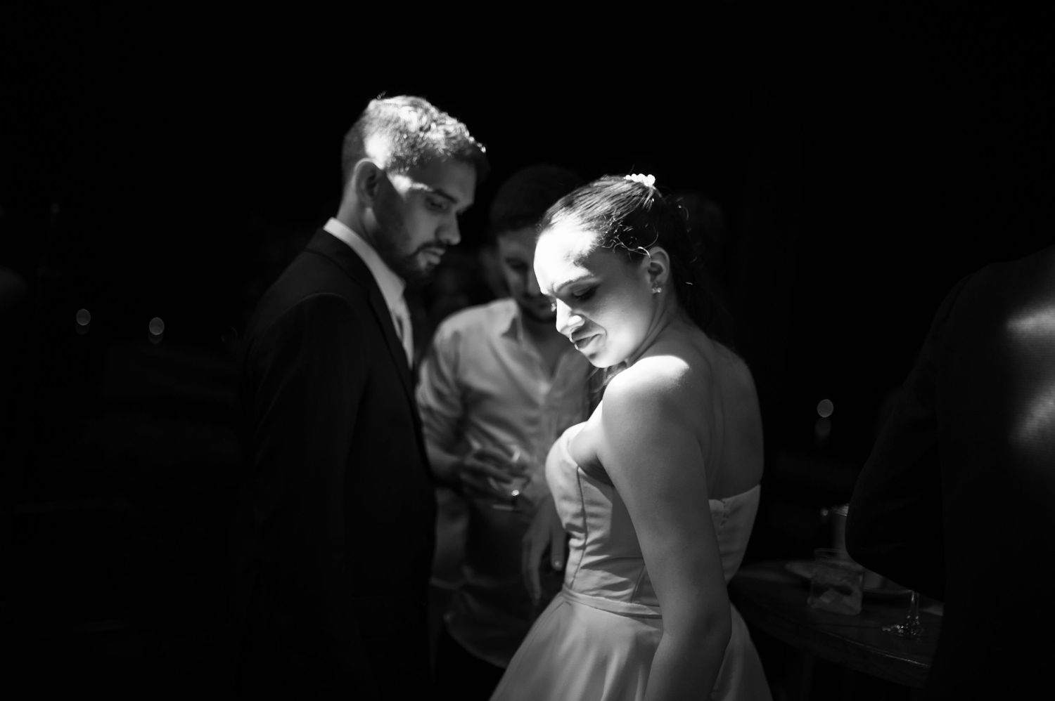 Black and white photo of a bride and groom at a wedding reception, sharing an intimate moment in dim lighting.
