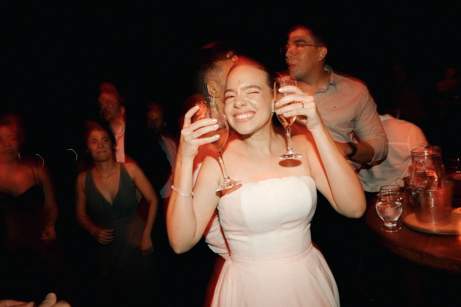 Smiling bride in white strapless dress holding champagne glass at wedding reception party.