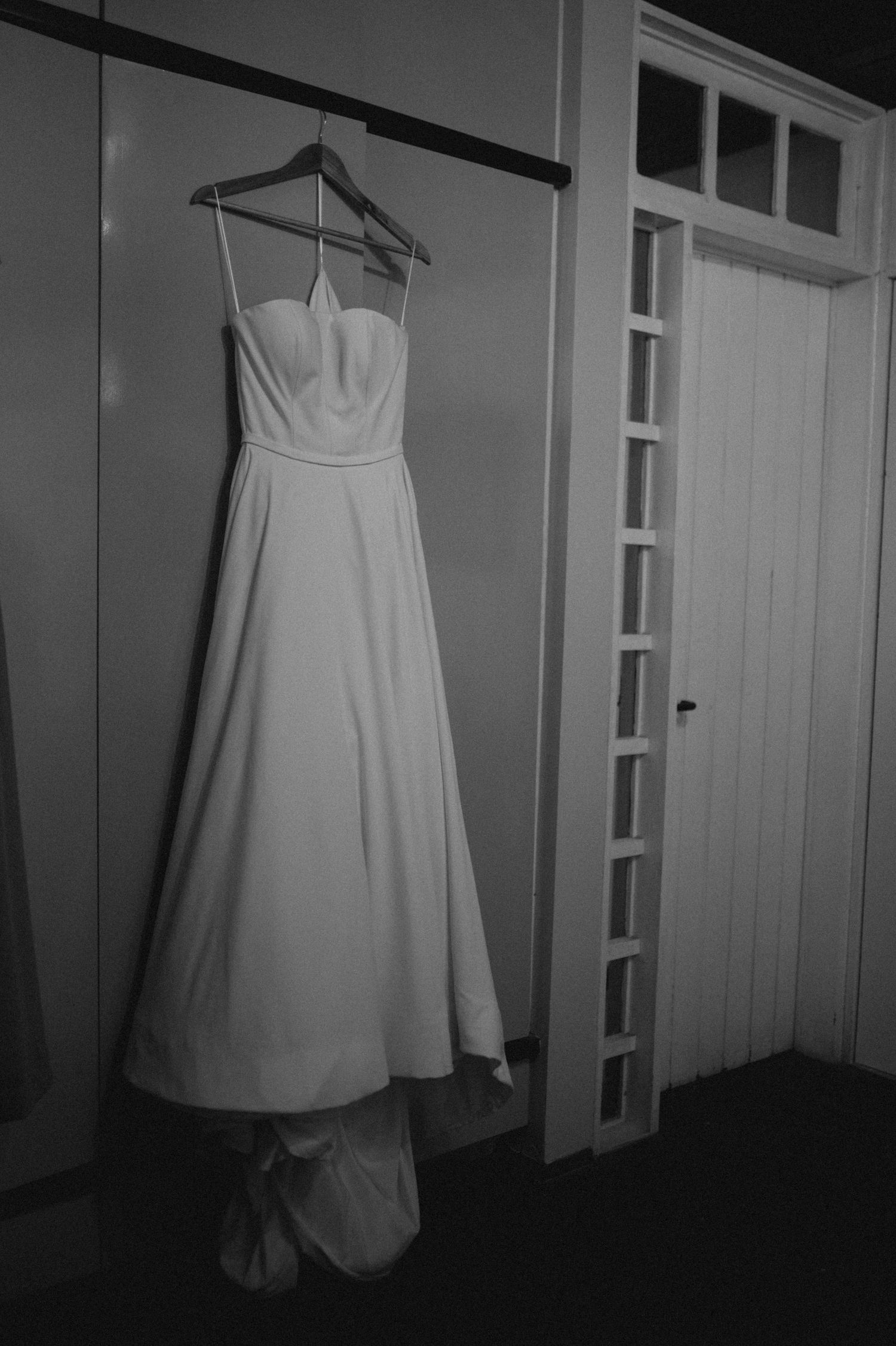Elegant white bridal gown with sweetheart neckline hanging on a hanger against a wooden door.
