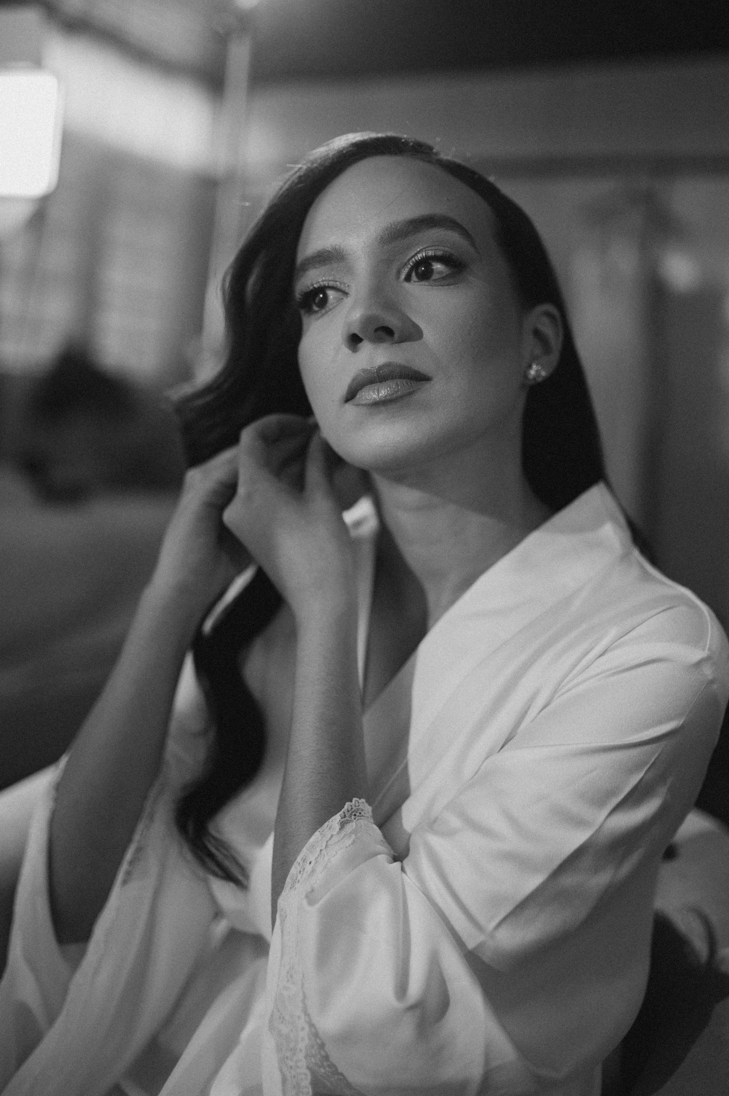 Black and white portrait of a woman in a white robe touching her earring, looking up elegantly.