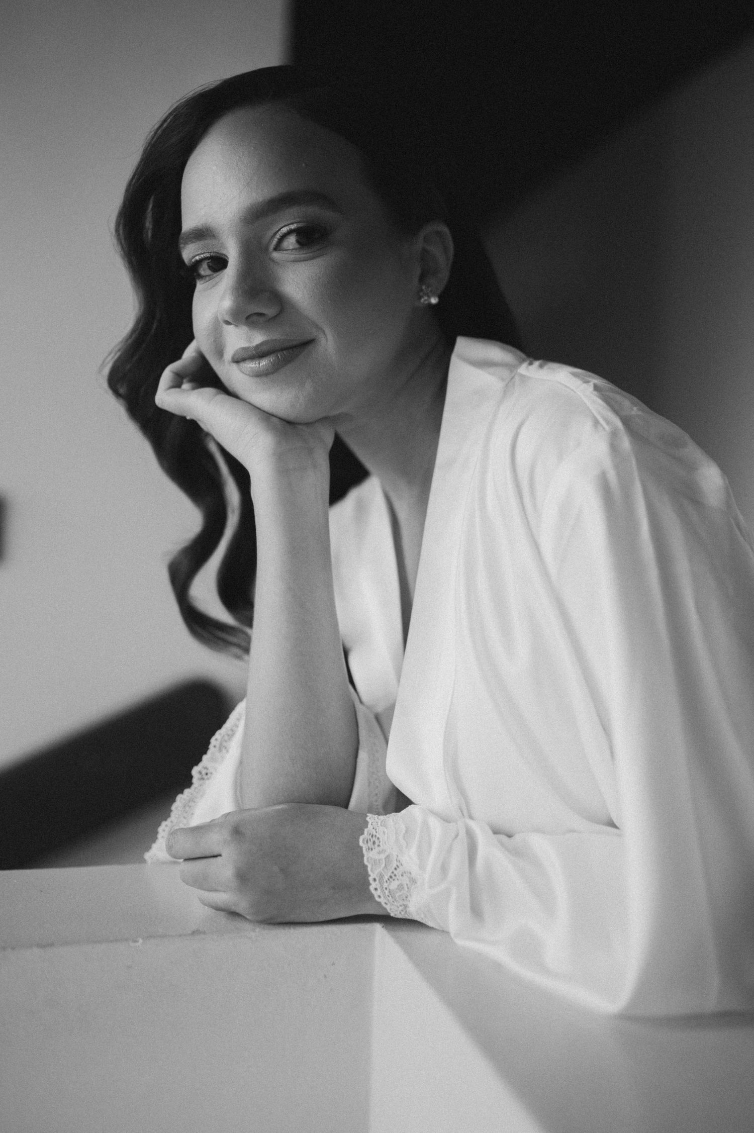 Black and white portrait of a smiling woman in a white robe resting her chin on her hand.