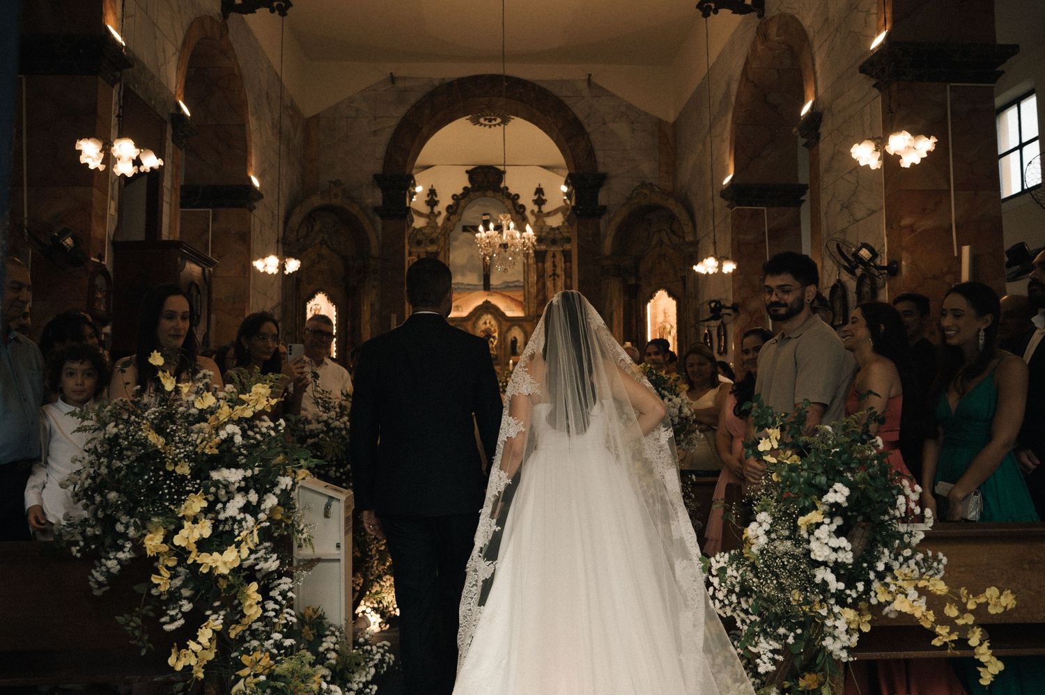 Bride and groom walking down the aisle of an ornate church decorated with white and yellow floral arrangements.