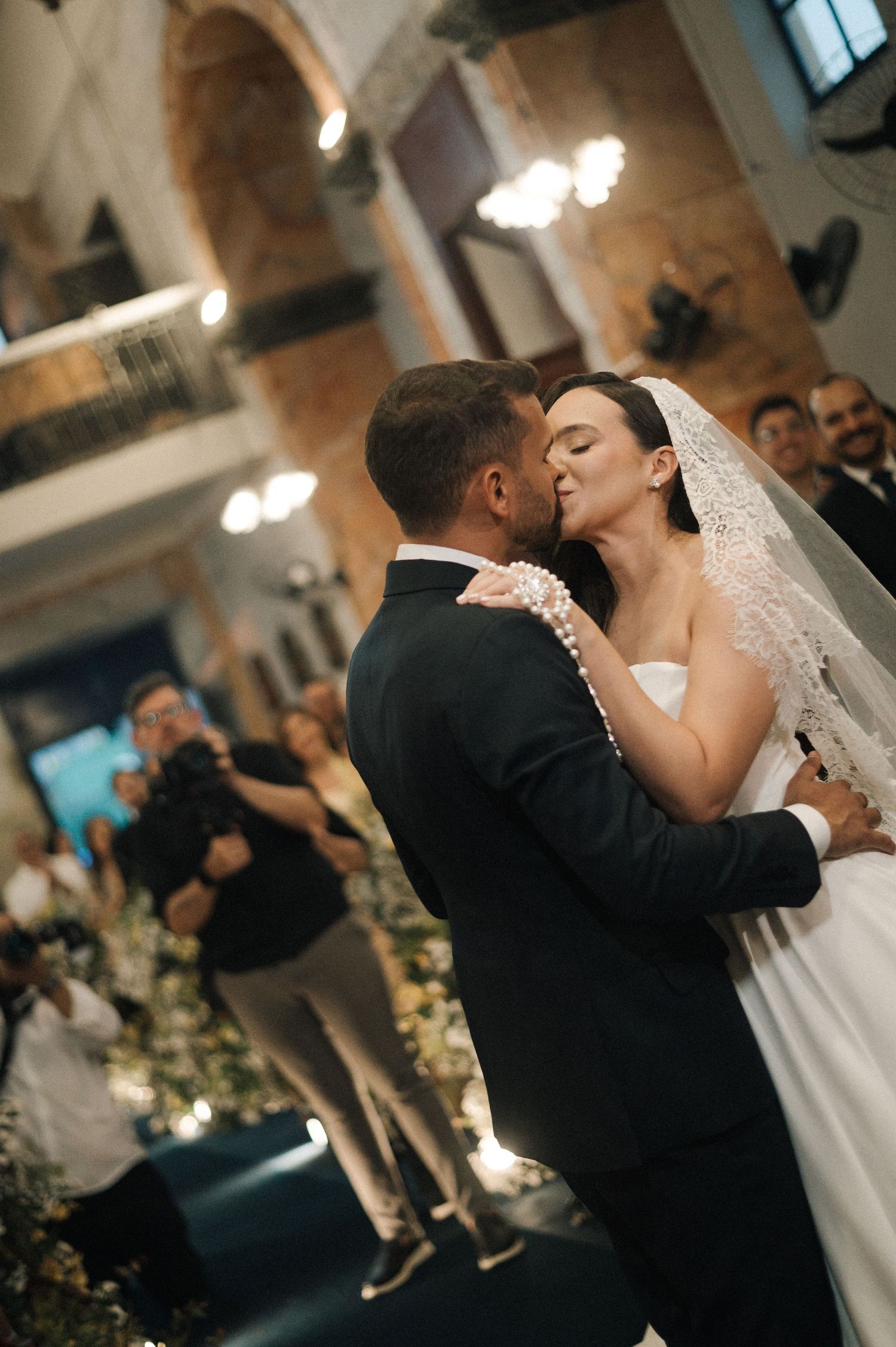 Bride and groom share their first kiss at the altar during an elegant church wedding ceremony with guests watching.