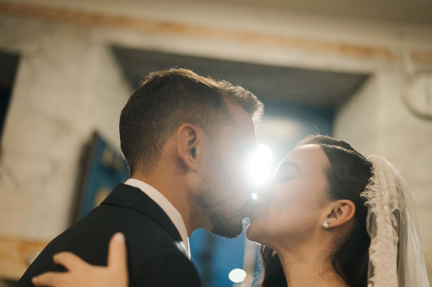 Bride and groom sharing a romantic first kiss at the altar, with a soft light glowing between them.