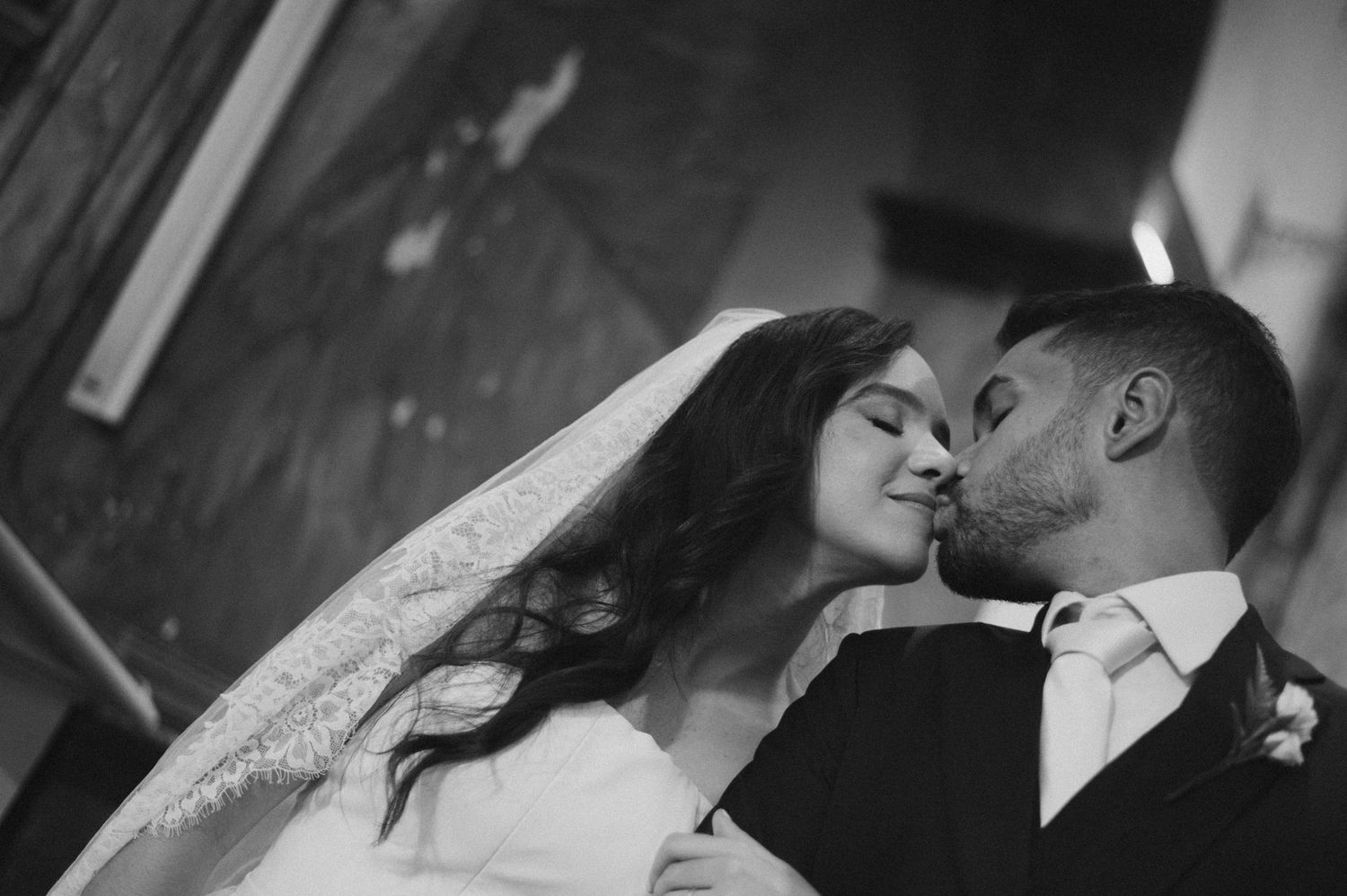 Black and white wedding photo of bride and groom sharing a romantic kiss, bride wearing veil.