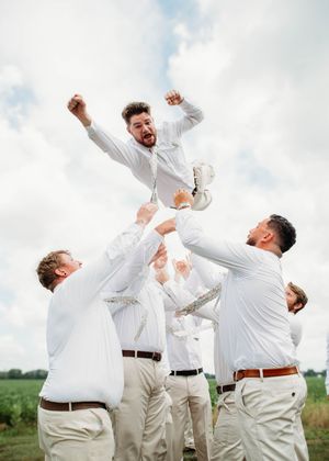 Groom doing spiderman pose while being tossed in the air, in Sherwood, MI