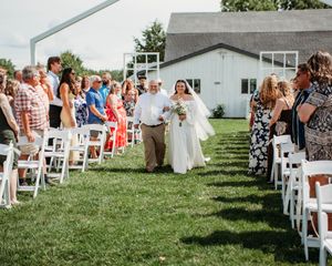 Bride walking down the aisle with Father of the bride during ceremony with wedding guest in white chairs in Sherwood,MI