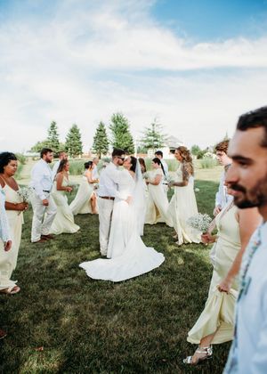 Bride and Groom kissing during portrait with bridesmaids ang groomsmen walking front of them for a unique photo in Sherwood,MI