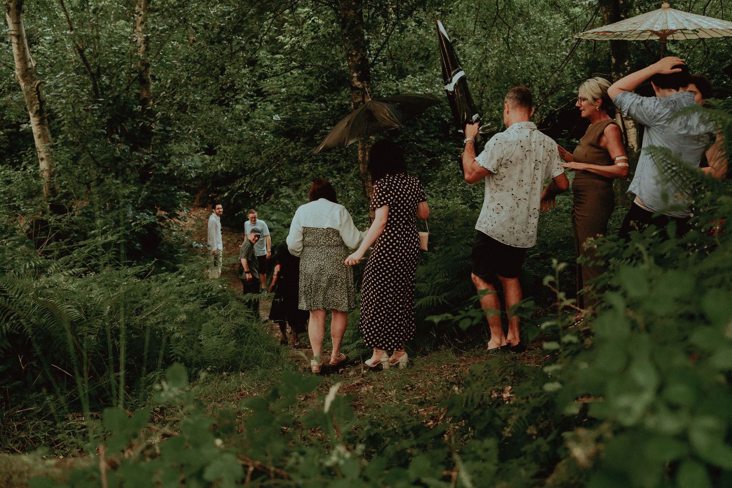 Guests walking through lush green woodland path at an outdoor wedding celebration.
