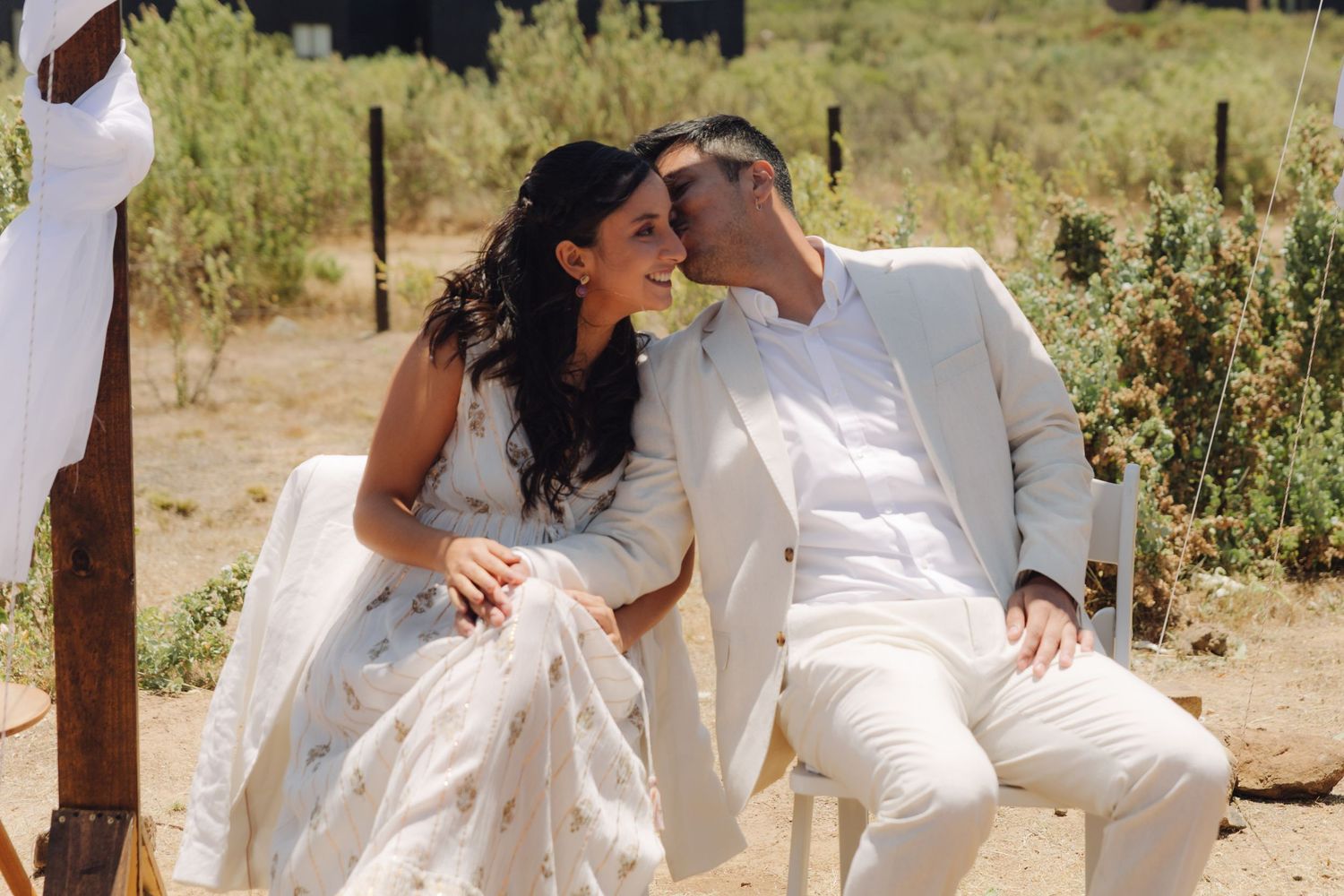 Happy bride and groom sitting together smiling at outdoor desert wedding.